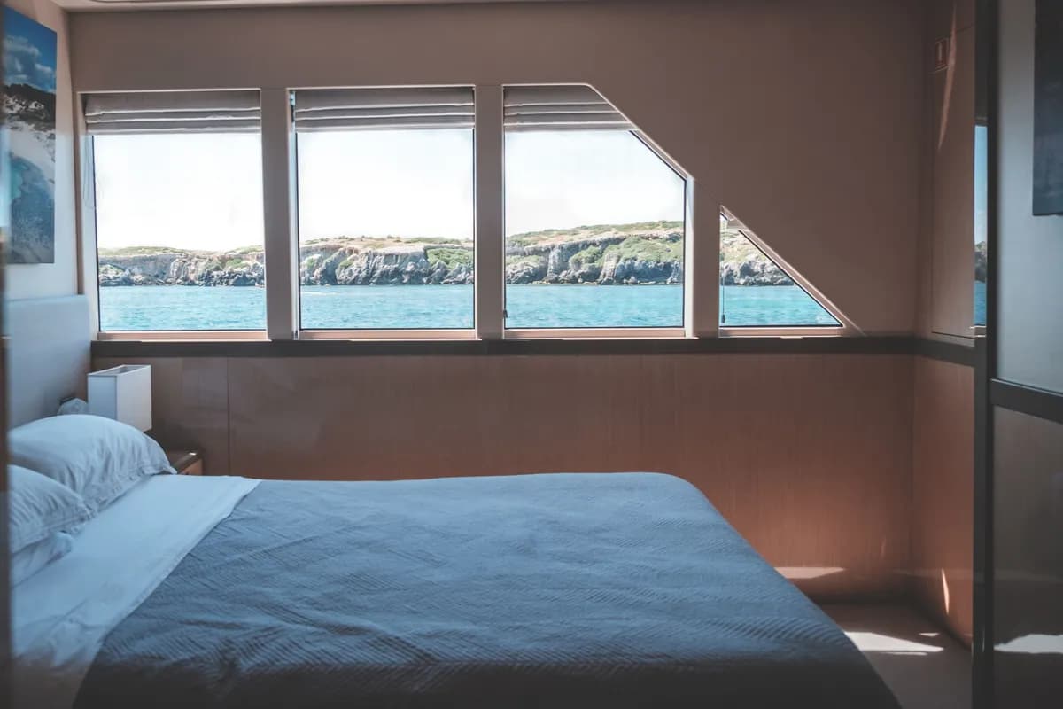 Imagen de ejemplo de BookNoFees: Cabina de barco luminosa con cama y grandes ventanas con vistas al mar