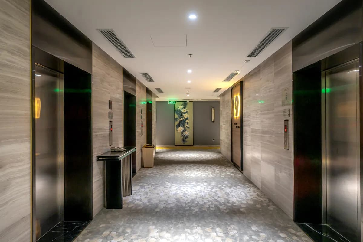 Imagen de ejemplo de BookNoFees: pasillo de hotel con ascensores y moqueta gris