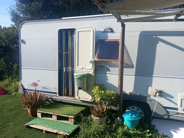 BookNoFees: alquiler vacacional en El Palmar De Vejer – Exterior de una caravana antigua con la puerta abierta, un toldo y plantas en macetas sobre el césped