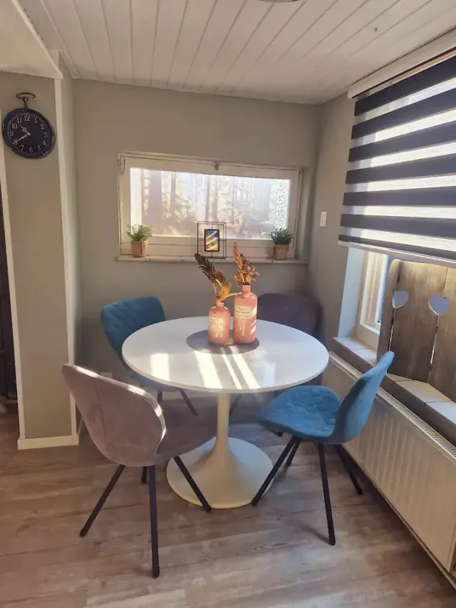 BookNoFees: alquiler vacacional en Domburg – Comedor con una mesa redonda blanca, sillas azules y grises, y una ventana con vistas al bosque