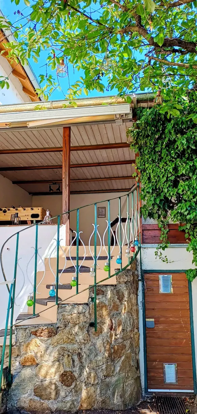 BookNoFees: alquiler vacacional en Straubing, Baviera, Alemania – Escalera exterior con pared de piedra, barandilla metálica y luces de cadena que conducen a una terraza cubierta con mesa de futbolín