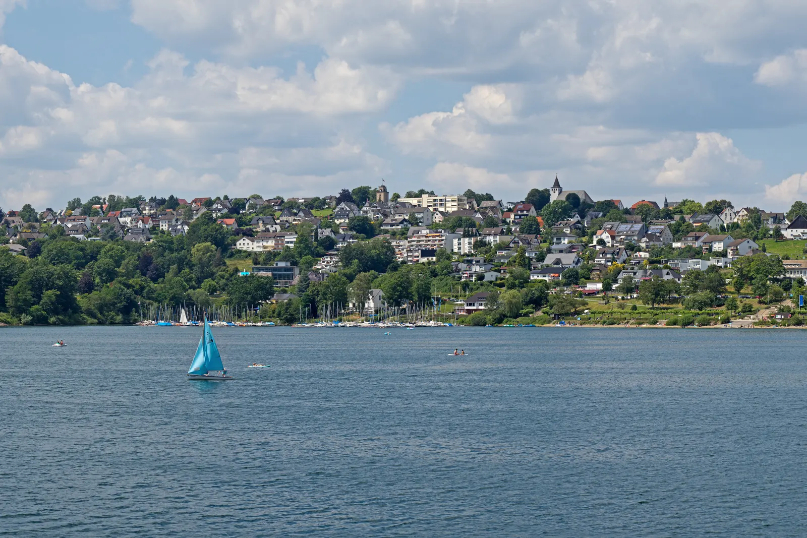 Langscheid, a orillas del Sorpesee, cerca de Sundern: el pueblo a orillas del lago, situado sobre el nivel del agua, con un velero al fondo