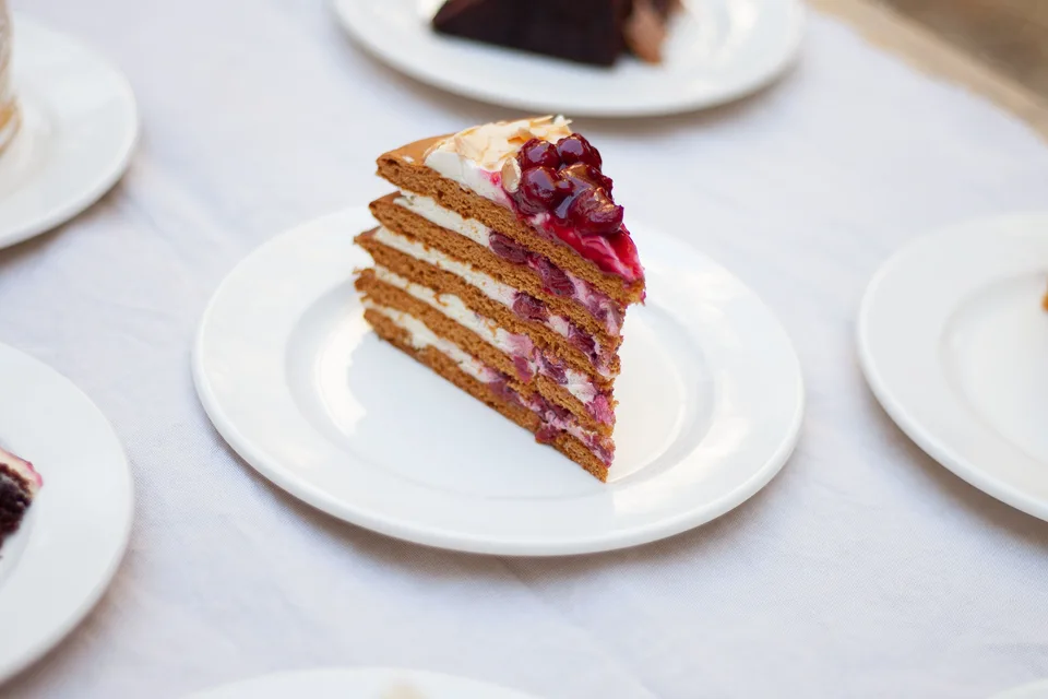 BookNoFees: Foto de ejemplo: Una porción de tarta de capas decorada con frutos del bosque en un plato blanco